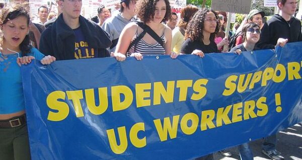 students marching behind a banner that reads students support UC workers