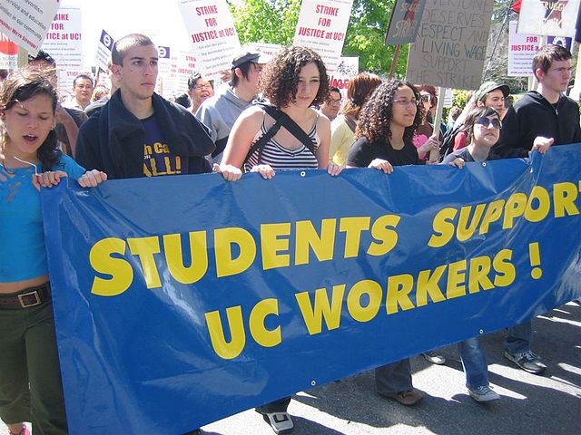 students marching behind a banner that reads students support UC workers